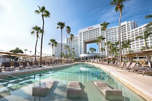 Un hotel con una piscina grande, palmeras y cielo despejado.