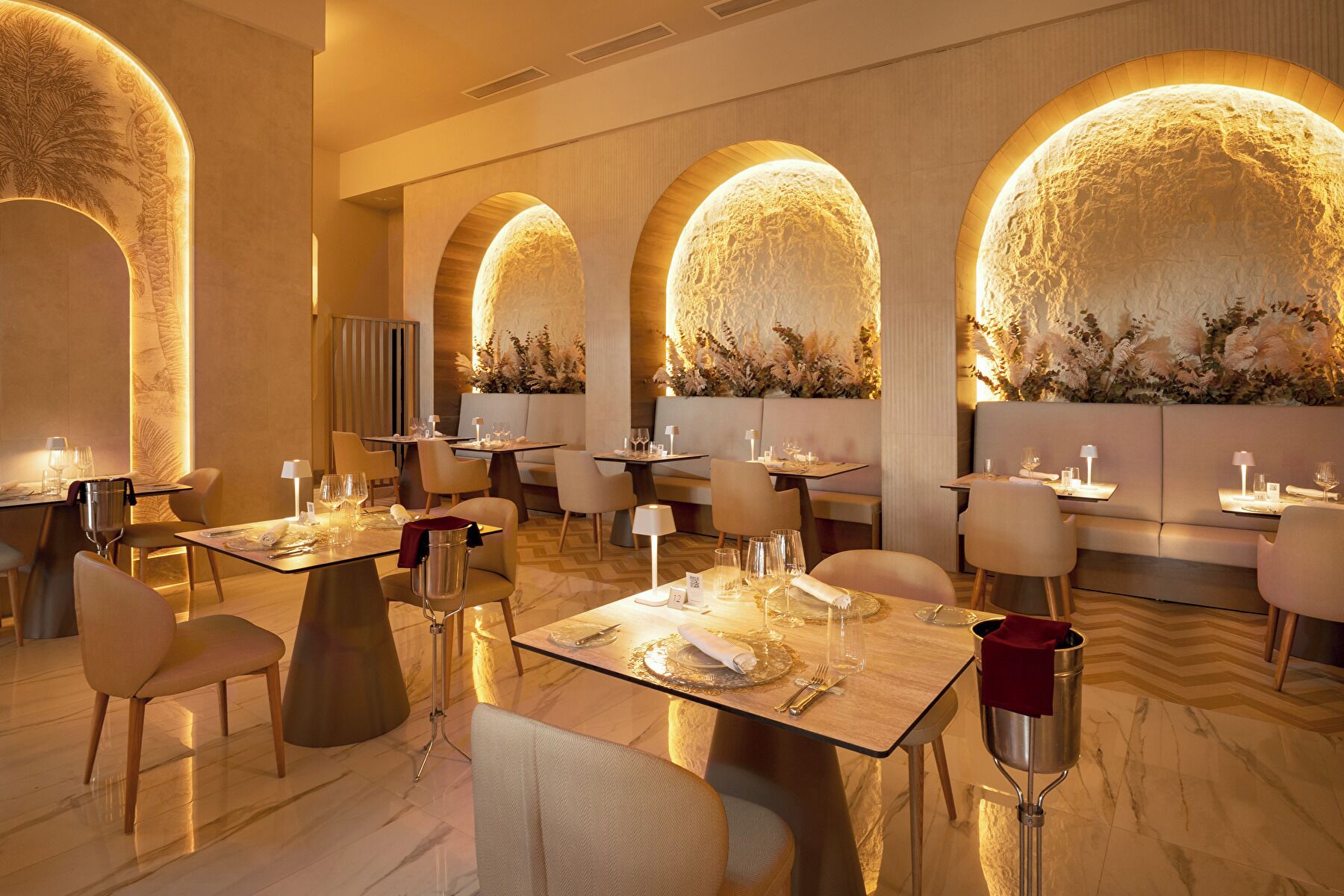 Un restaurant doté de nombreuses tables, de chaises et d’un mur chaleureux, illuminé d’une lumière douce.