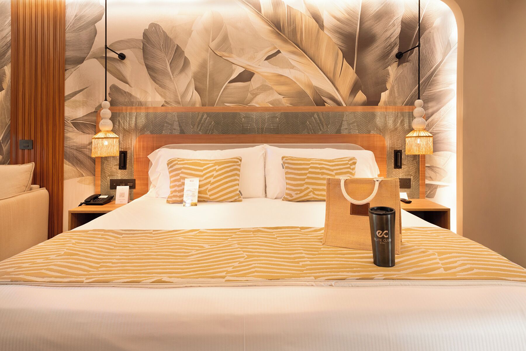 Una habitación de hotel con una cama grande, dos mesitas de noche, una lámpara y una pared con un diseño de hojas.