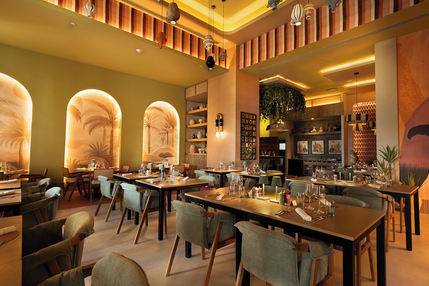 A restaurant interior with multiple dining tables, chairs, and a variety of decorative elements including wall art and lighting fixtures.