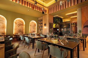 Ein Restaurantinneres mit mehreren Esstischen, Stühlen und verschiedenen Dekorationselementen, darunter Wandbilder und Leuchten.