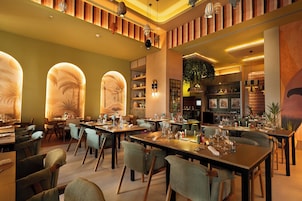 Interior de restaurante con varias mesas, sillas y distintos elementos decorativos, incluyendo cuadros y lámparas.
