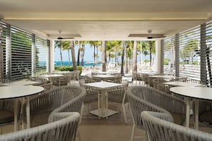 A beachside restaurant with outdoor seating, palm trees, and a view of the ocean. - Hotel Riu Palace Peninsula - All Inclusive (Cancun)