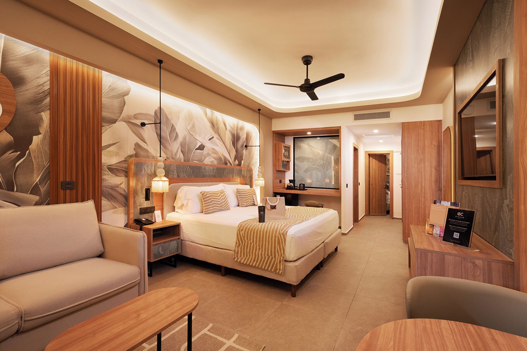 Habitación de hotel con cama, escritorio, silla, sofá, ventilador de techo y un espejo grande.