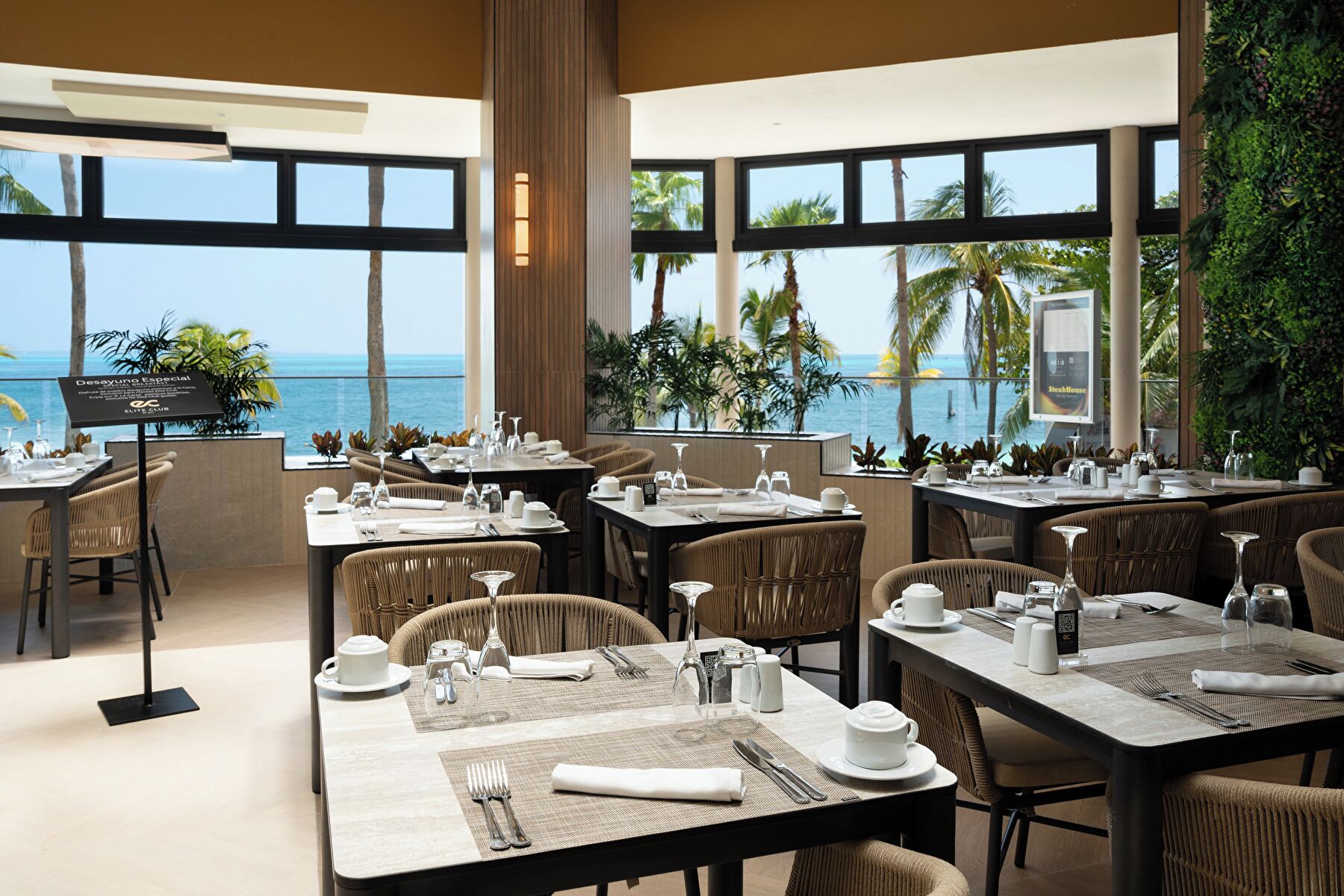 A restaurant with tables set for dining, large windows offering a view of the ocean, and a sign indicating a special dining option.