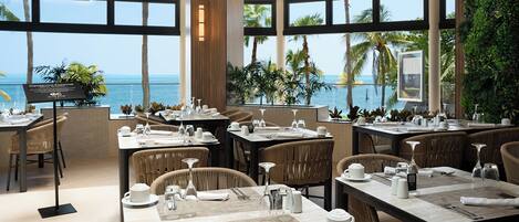 A restaurant with tables set for dining, large windows offering a view of the ocean, and a sign indicating a special dining option.