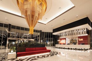 Un moderno hall de hotel con un mostrador de recepción, un sofá rojo y una gran araña.