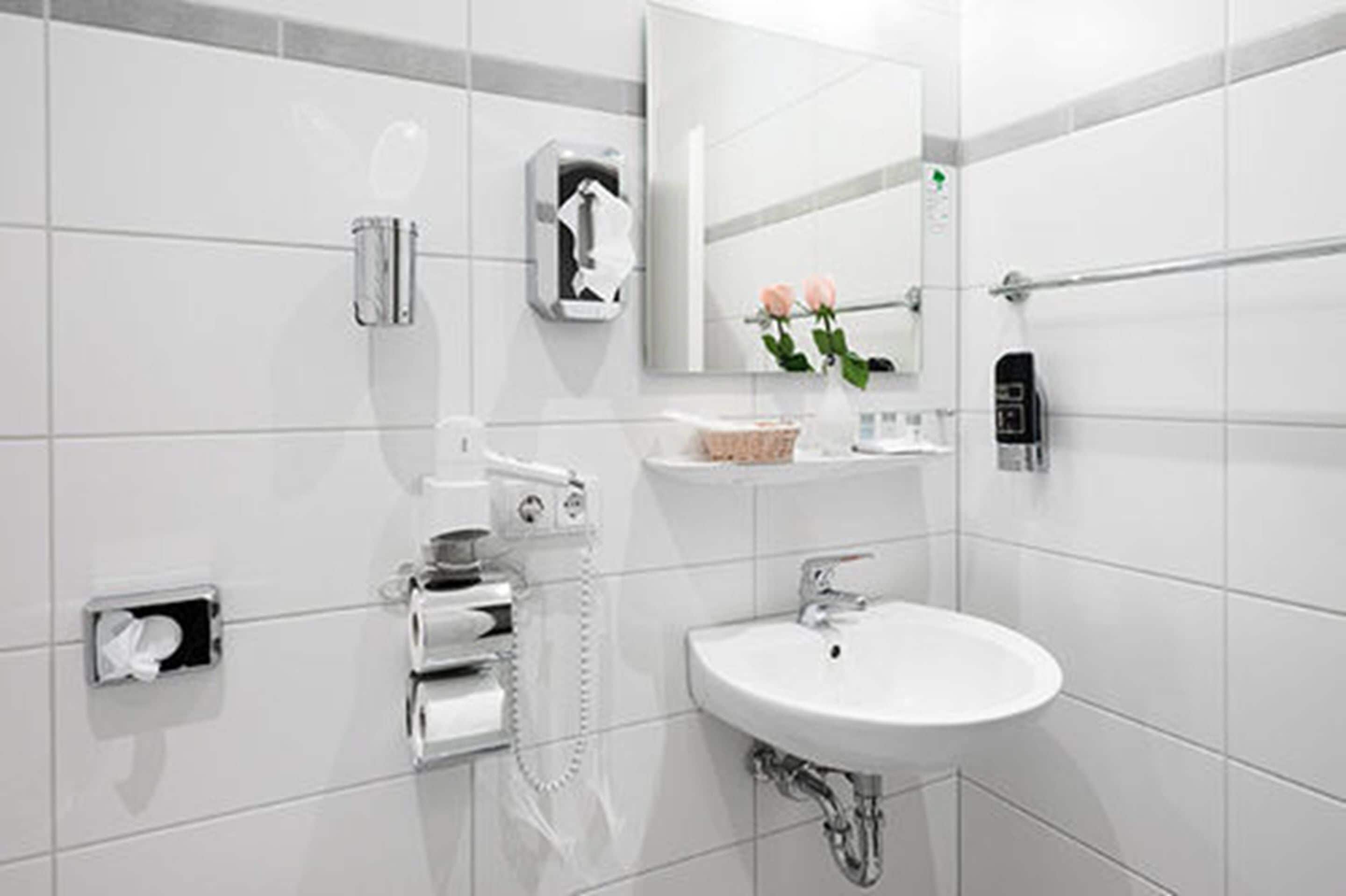 Un baño moderno con lavamanos blanco, espejo, dispensador de toallas y dispensador de jabón.