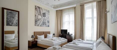 Quarto de hotel com duas camas de solteiro, uma cama de casal, uma escrivaninha com cadeira, televisão e uma janela grande com cortinas.