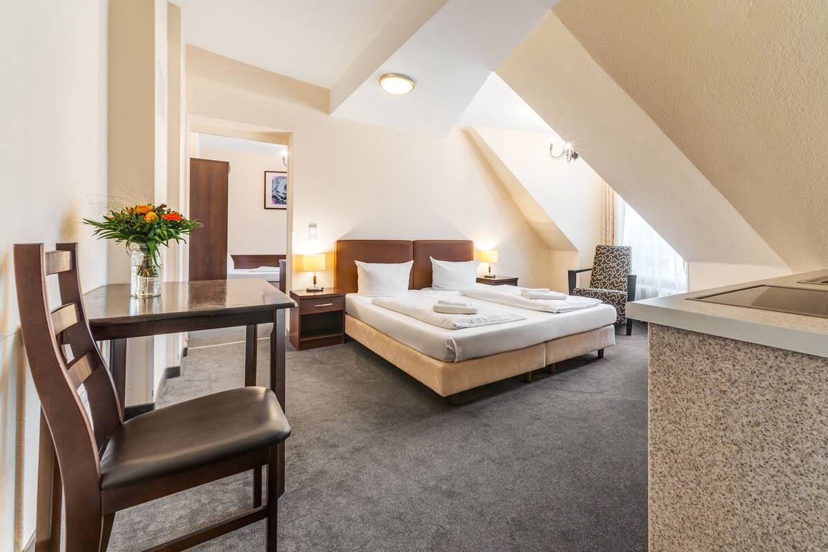 Una camera d'albergo con un letto, comodini, una scrivania, una sedia e un vaso con fiori.