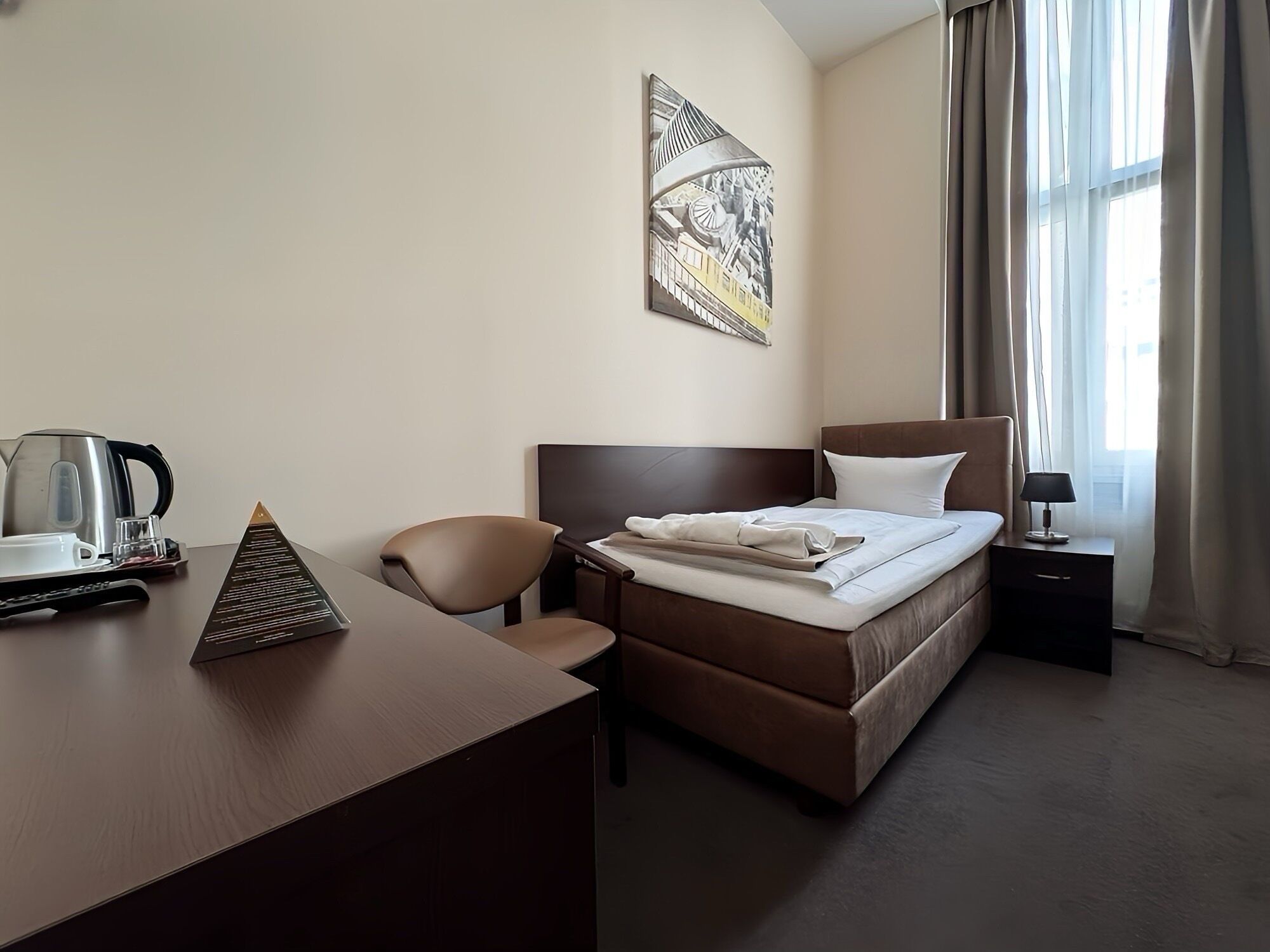 Ett hotellrum med en säng, ett skrivbord, en stol, en kaffebryggare och en lampa.
