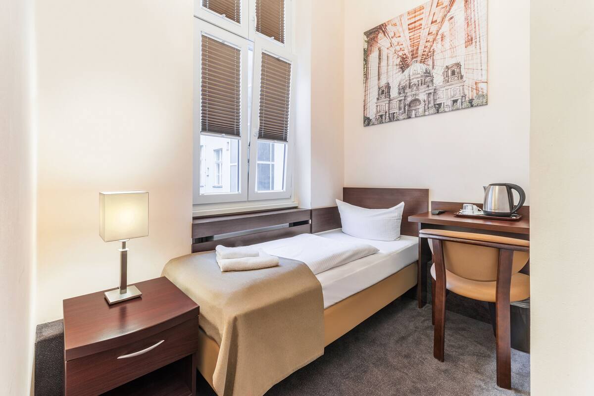 Una camera d'albergo con un letto, un comodino, una lampada, una sedia e un quadro appeso al muro.