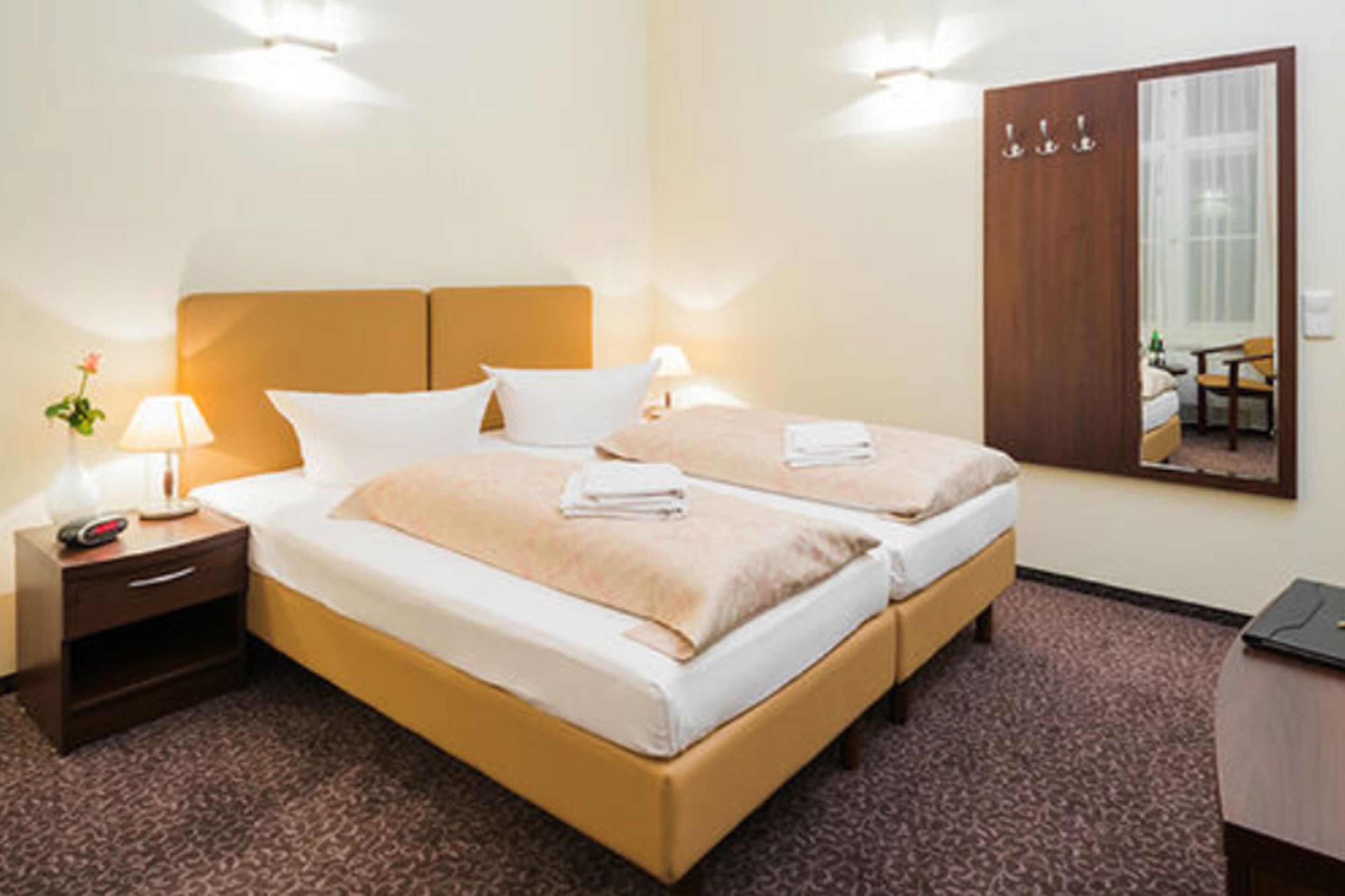 Habitación de hotel con dos camas, una mesita de noche con lámpara, un armario y un espejo.
