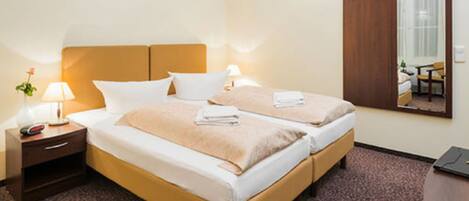 Habitación de hotel con dos camas, una mesita de noche con lámpara, un armario y un espejo.