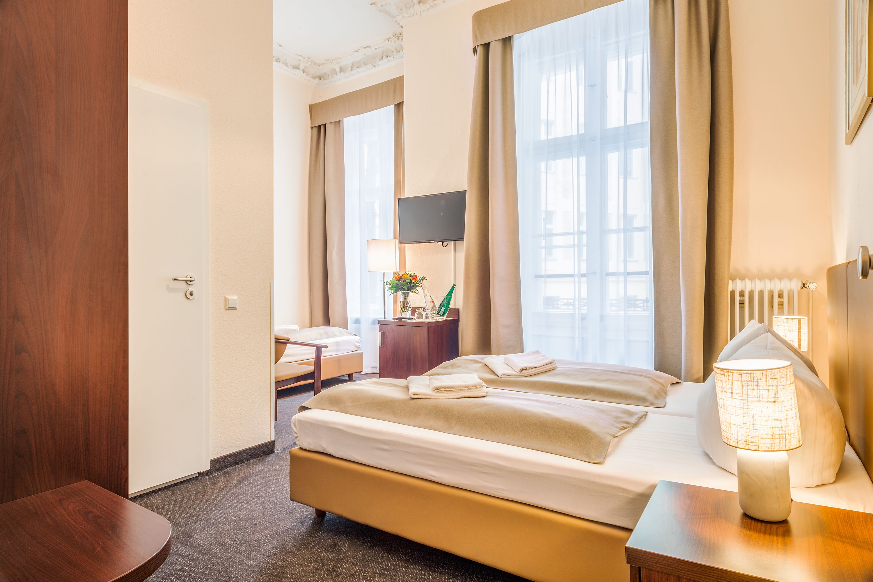 A hotel room with a bed, bedside table, lamp, and a desk with a chair.