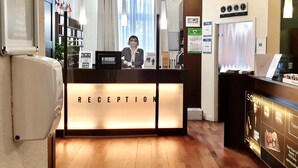 A reception area with a reception desk labeled "RECEPTION," a chandelier, and a wall clock. - Upper Room Hotel Kurfurstendamm (Berlin)