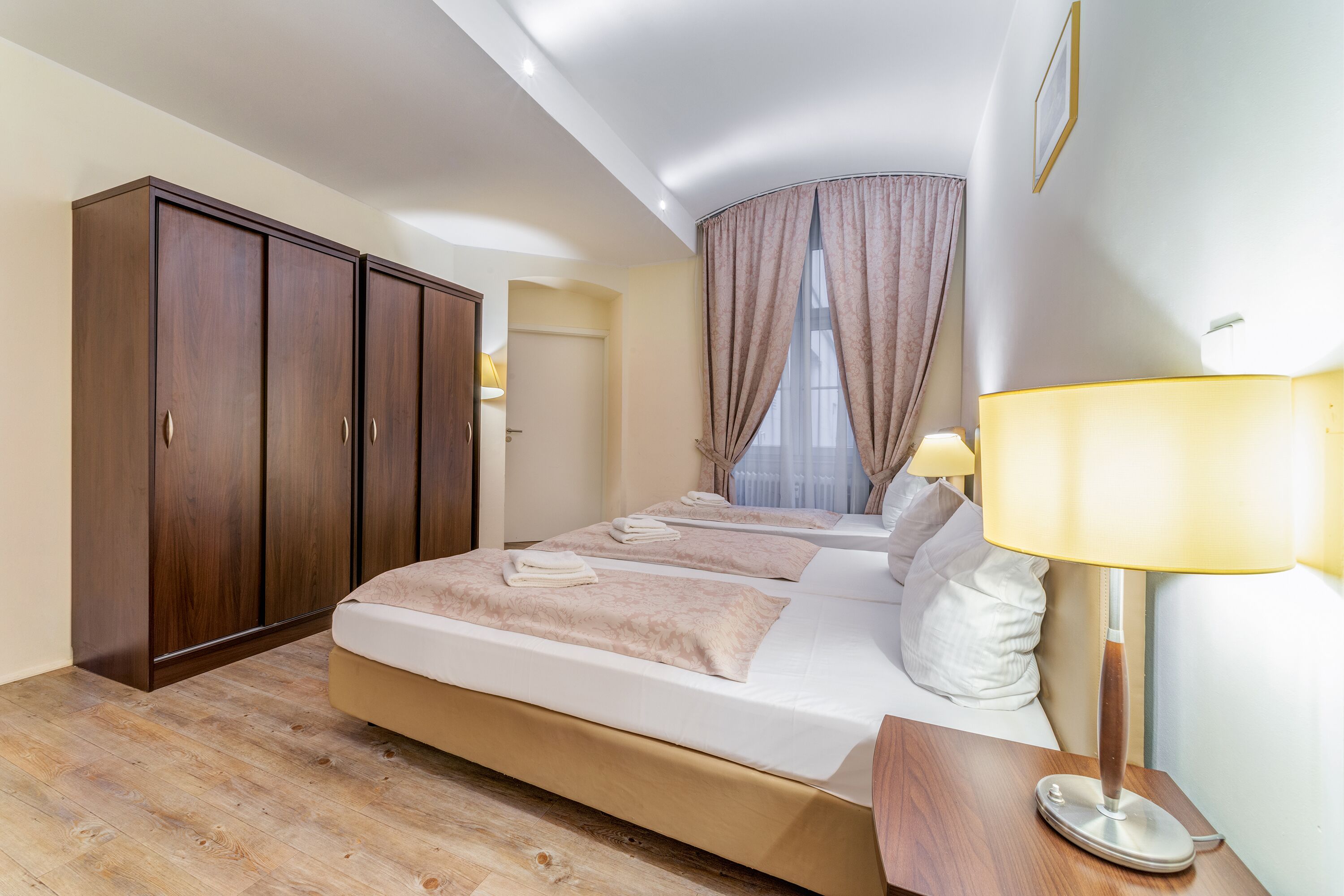 A hotel room with a large bed, wooden wardrobe, and a bedside lamp.