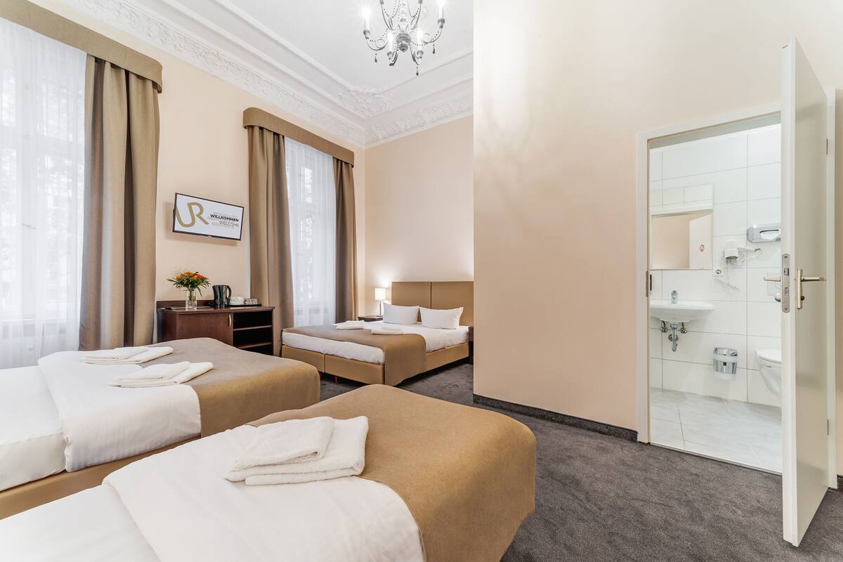 Camera d'albergo con due letti, una scrivania, una sedia, un lampadario e un bagno con lavandino e specchio.