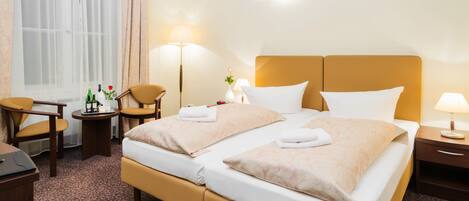 Una habitación de hotel con cama doble, dos mesitas de noche, un escritorio con silla, una lámpara y una ventana con cortinas.