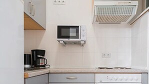 A compact kitchen with white cabinets, a microwave, a stove, and a coffee maker. - Upper Room Hotel Kurfurstendamm (Berlin)