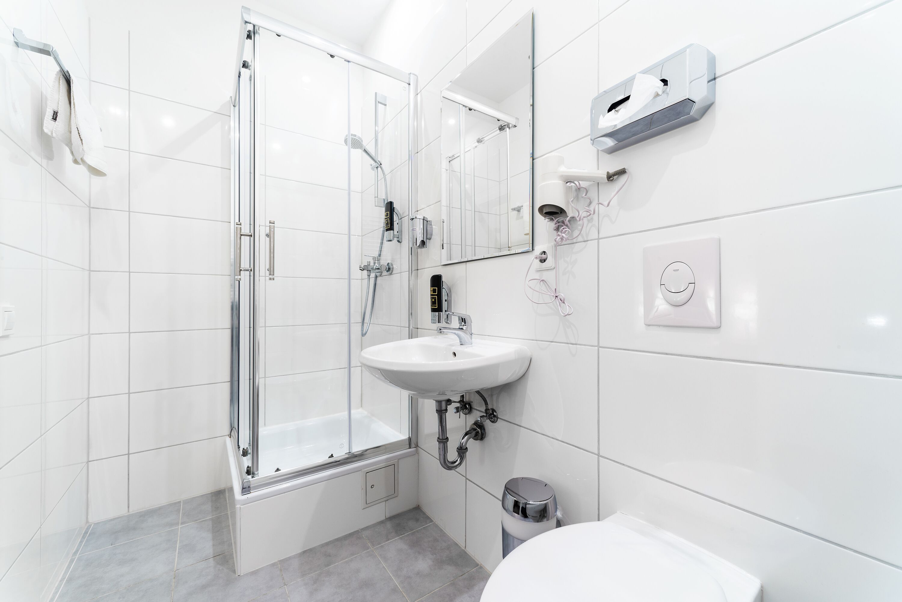 Ein modernes Badezimmer mit einer Glaskabine zur Dusche, einem weißen Waschbecken und einem Spiegel.