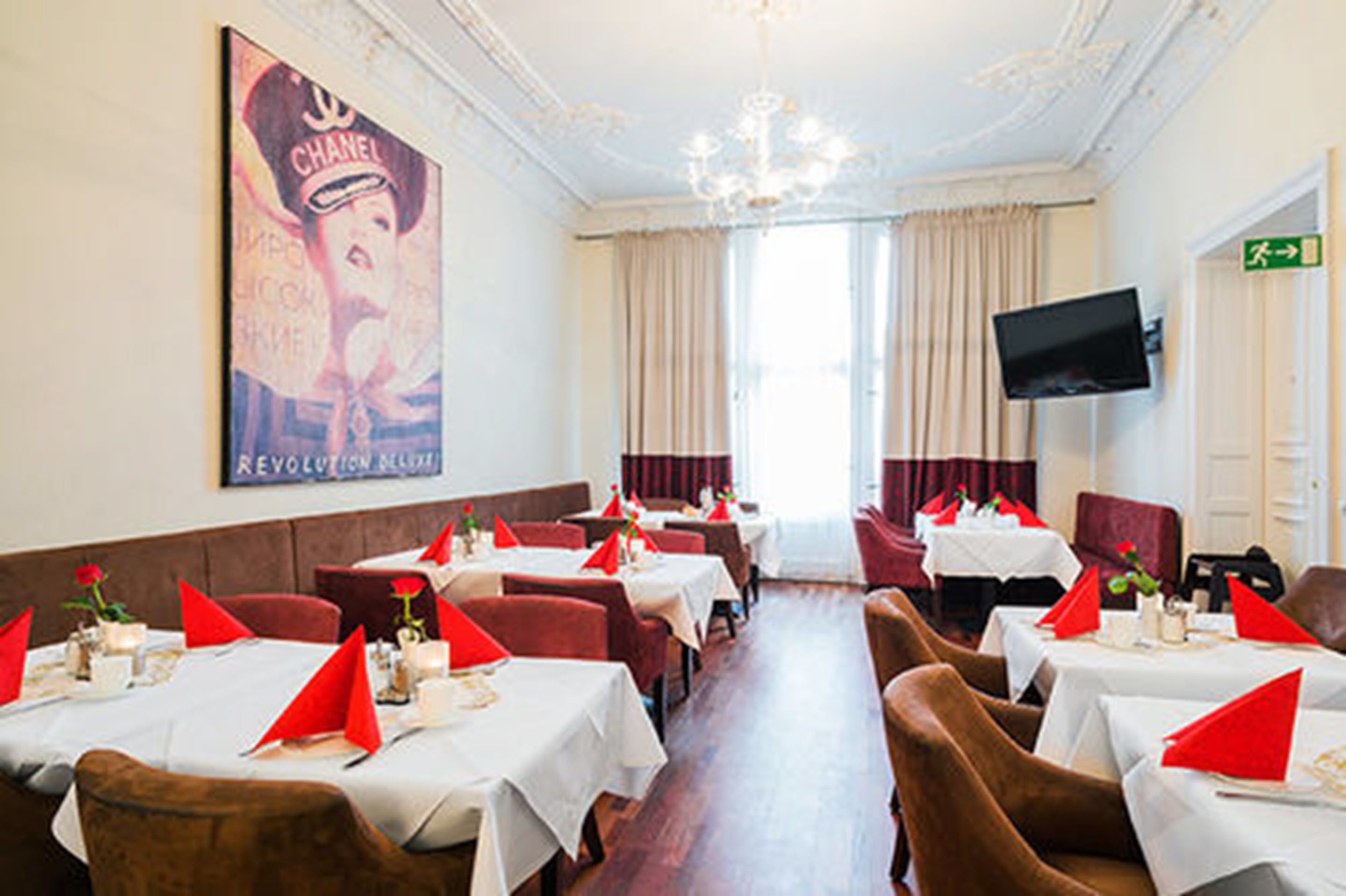 A restaurant with tables set for dining, a chandelier, and a poster on the wall.