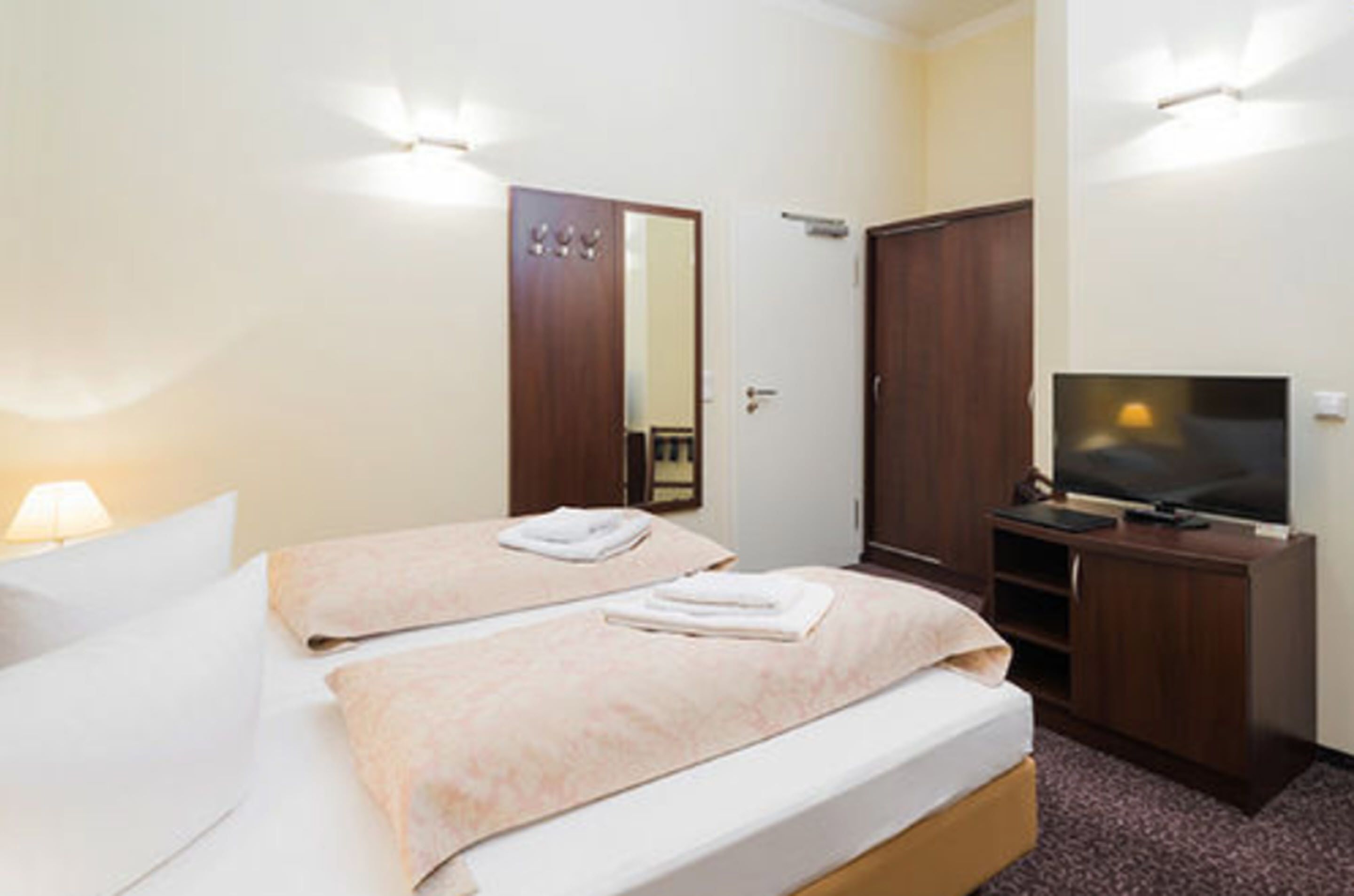 Habitación de hotel con dos camas, televisión, armario y espejo.