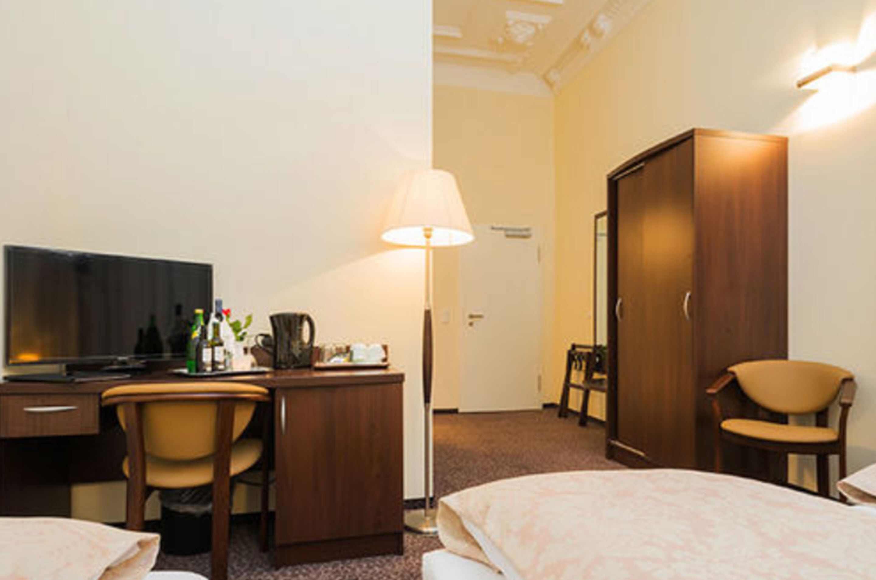 A hotel room with a bed, a desk with a television, a lamp, and a wardrobe.