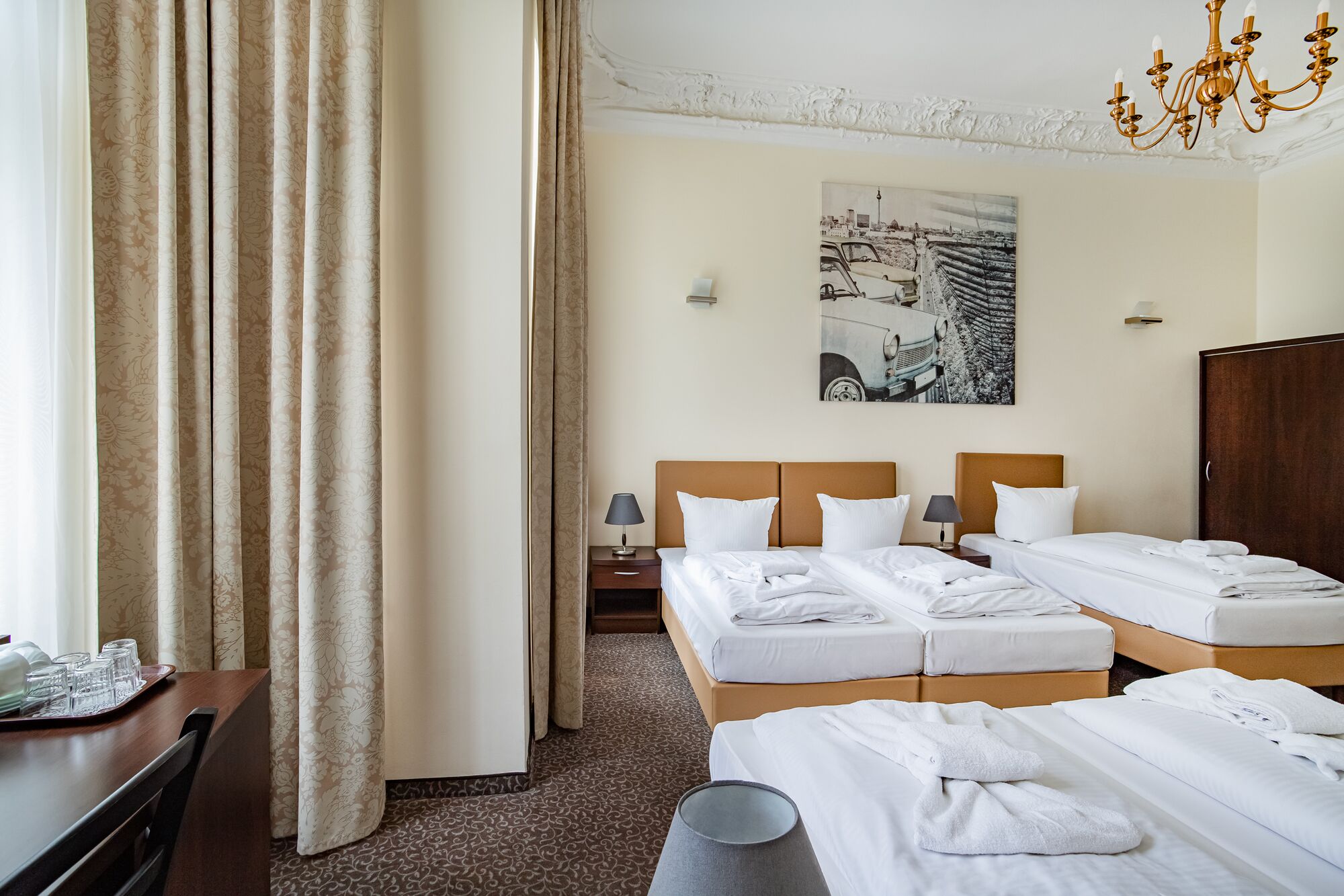 Une chambre d’hôtel avec deux lits, une table à manger avec des verres, une lampe et un tableau au mur.