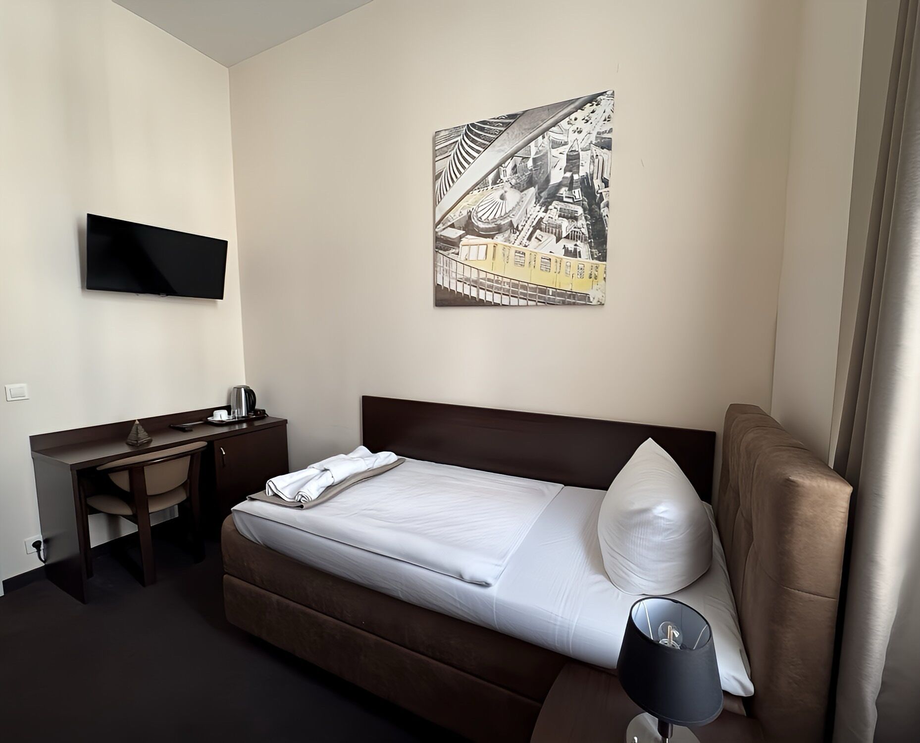 Hotellihuone, jossa on sänky, työpöytä, tuoli, televisio ja taulu seinällä.