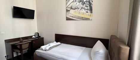 Hotellihuone, jossa on sänky, työpöytä, tuoli, televisio ja taulu seinällä.