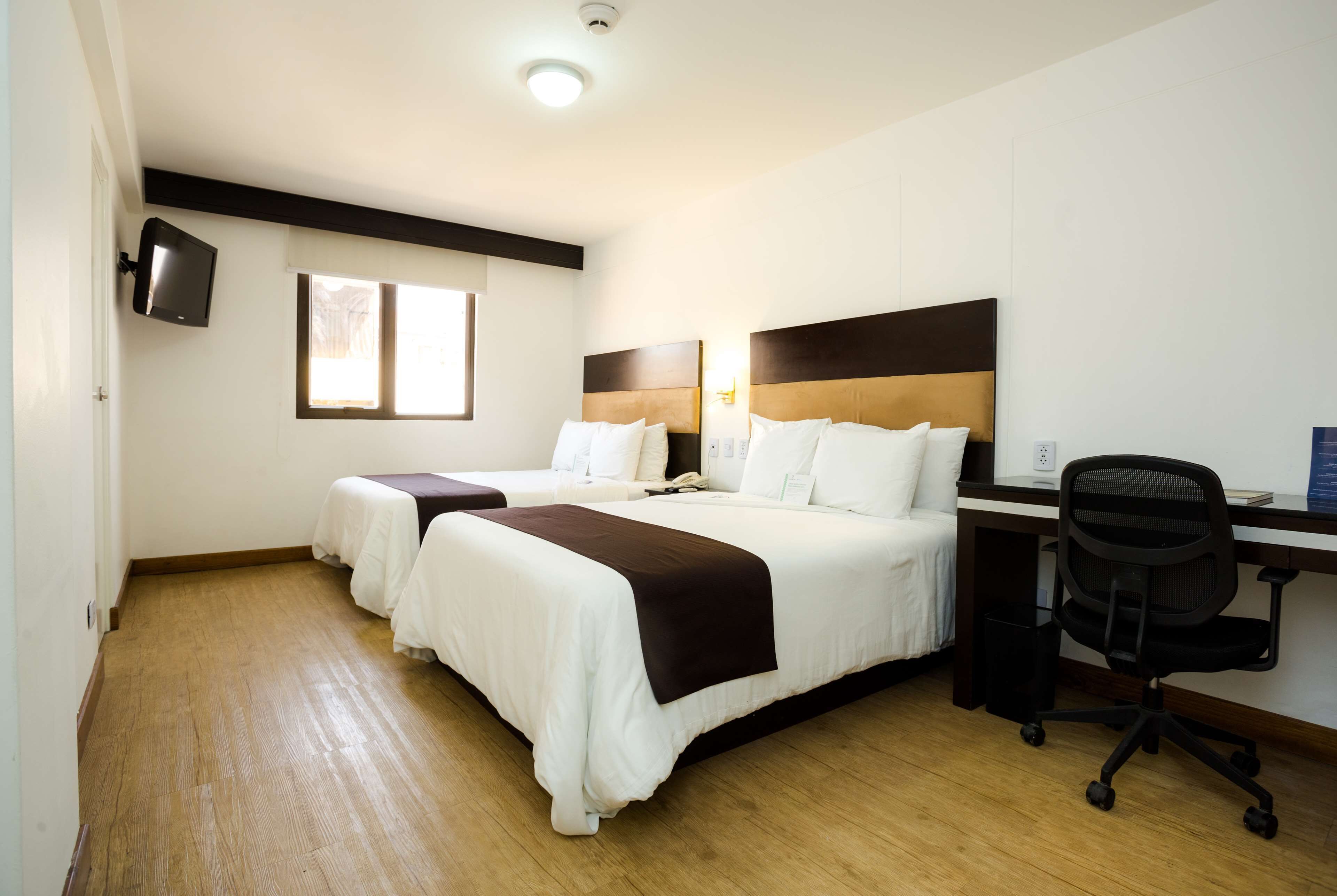 Habitación de hotel con dos camas, un escritorio, una silla, un televisor y una ventana.
