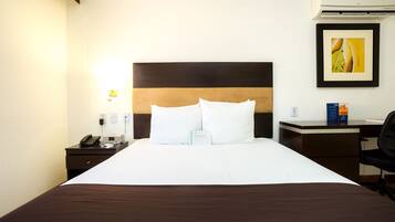 A hotel room with a large bed, a desk, a chair, a phone, and a framed picture on the wall.