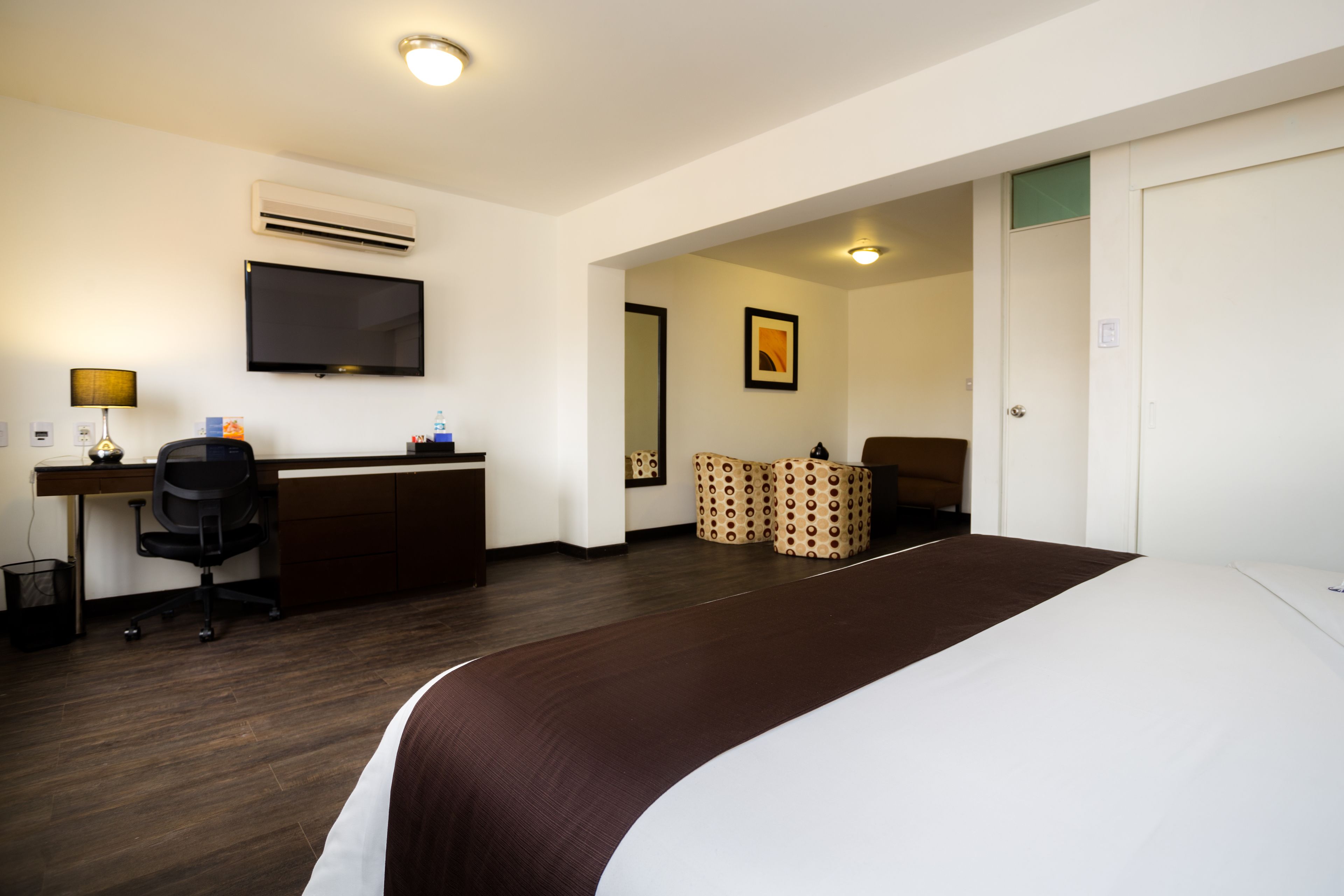 Habitació d'hotel amb un llit gran, un escriptori amb un ordinador, una cadira, un televisor i una porta que dona a una altra habitació.