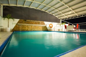 Une piscine intérieure dotée d’un sol carrelé, d’un mur en pierre et d’une structure de toit couverte.