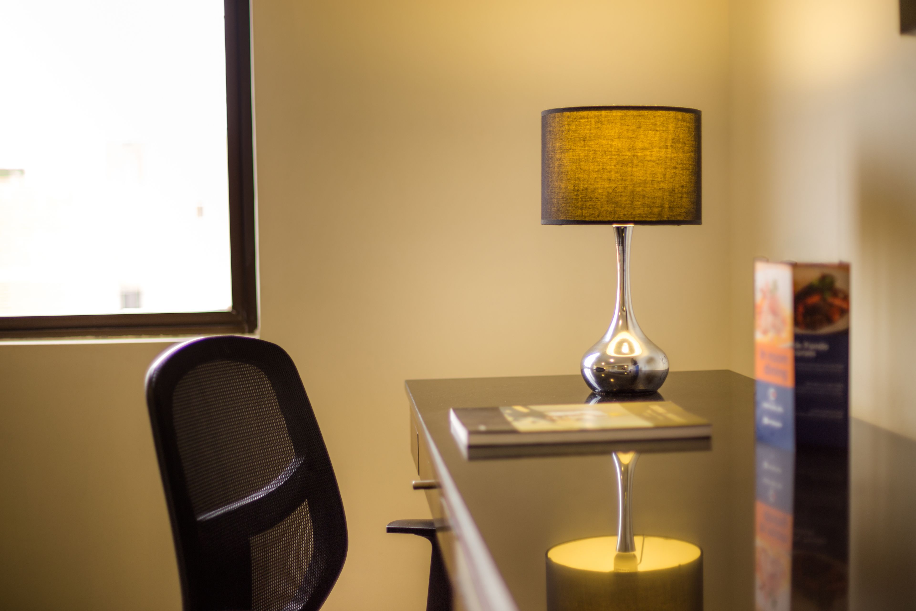 A desk with a lamp, a chair, and a window.