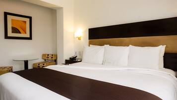 A hotel room with a large bed, a bedside table, a chair, and a wall-mounted light.
