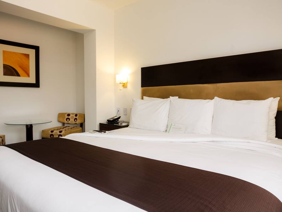A hotel room with a large bed, a bedside table, a chair, and a wall-mounted light.