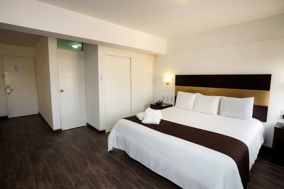 A hotel room with a large bed, a bedside table, a nightstand, and a wardrobe.