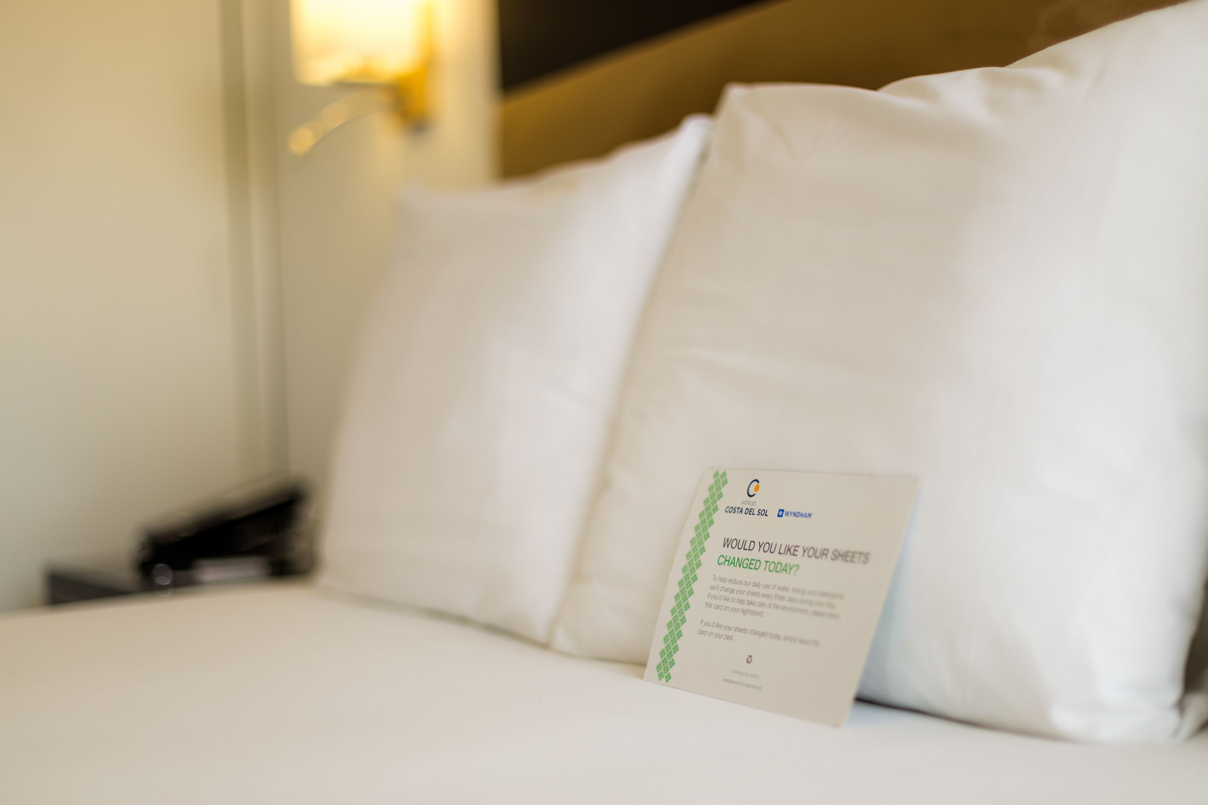 Een hotelbed met witte lakens en een brochure erop.