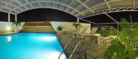 Une piscine intérieure avec un mur en pierre et une structure de toit en métal.