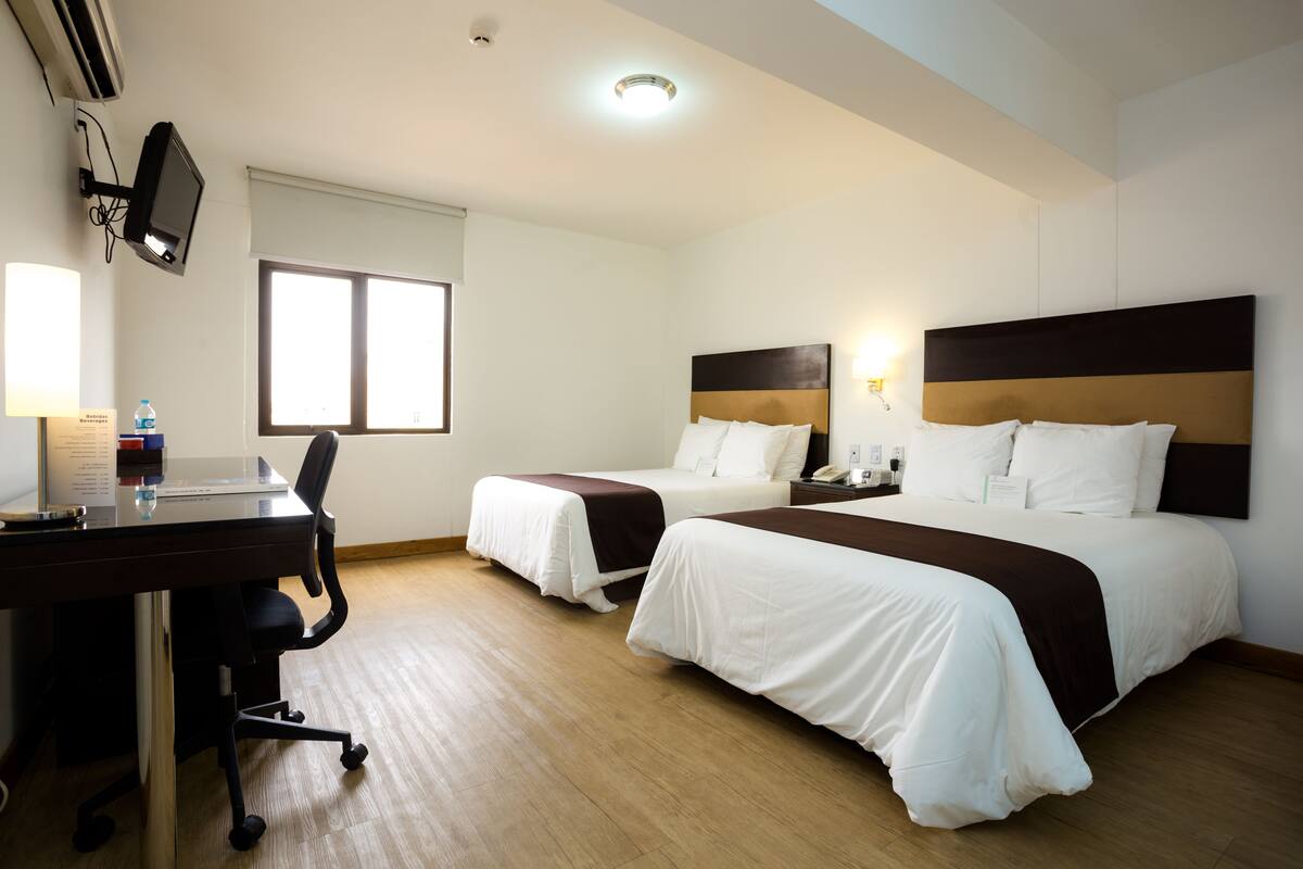 A hotel room with two beds, a desk, and a chair.