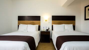A hotel room with two beds, each with white linens and brown headboards. There is a nightstand between the beds with a phone and a small table.