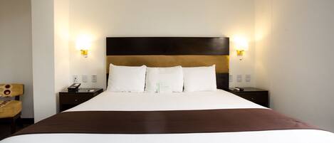 Habitación de hotel con una cama grande, dos mesitas de noche, una silla y lámparas fijadas a la pared.