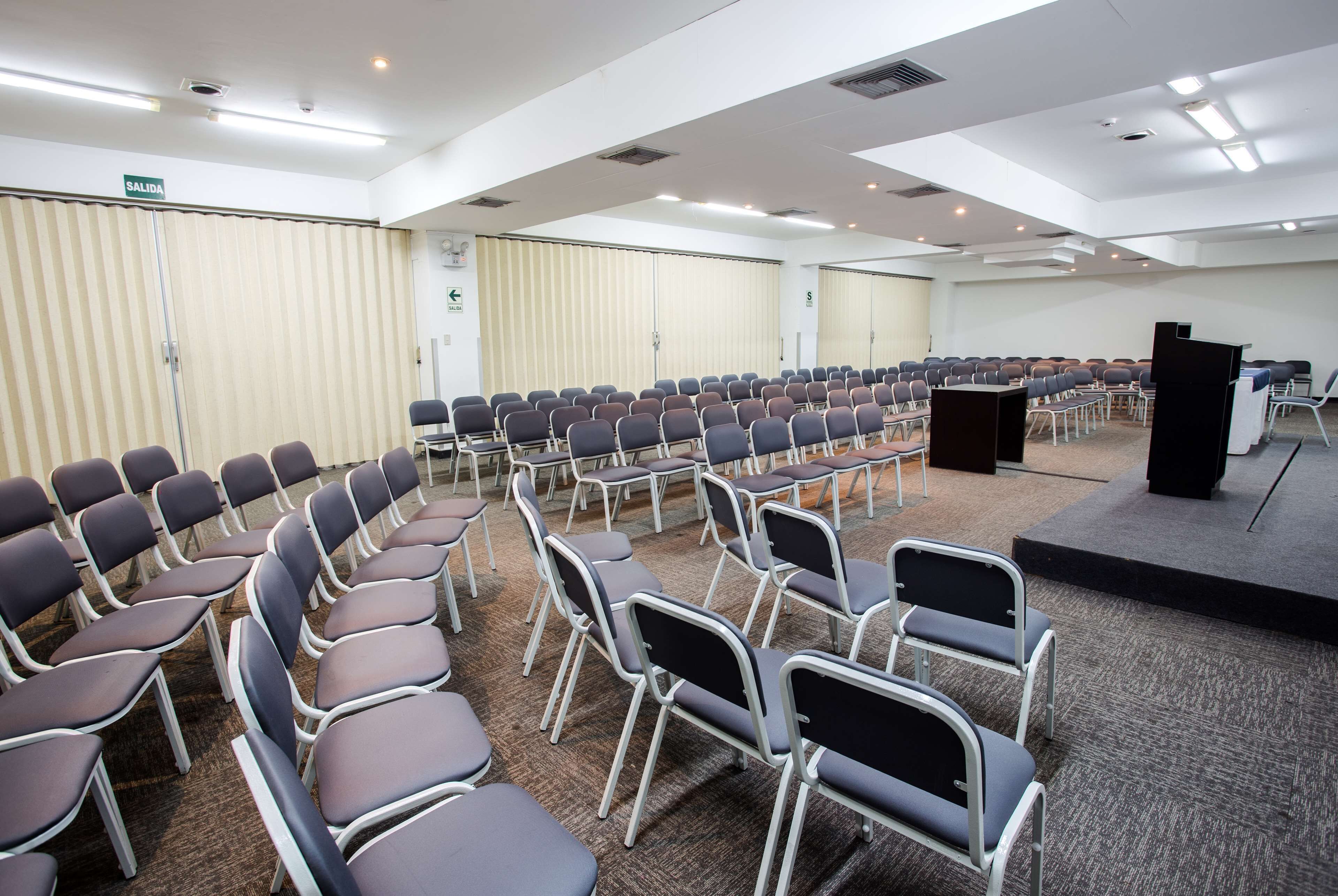 A conference room with rows of chairs, a podium, and a sign indicating the exit.
