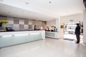 Un área de recepción de hotel moderna con entrada por puerta de vidrio, mostrador de recepción y zona de espera.