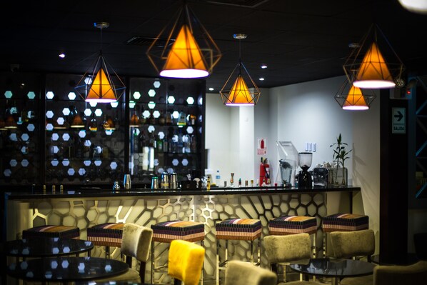 A bar area with hexagonal patterned wall, multiple stools, and hanging pendant lights.