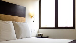 A hotel room with a bed, a nightstand, a wall-mounted lamp, and a window. - Wyndham Costa del Sol Chiclayo - Chiclayo (Chiclayo)