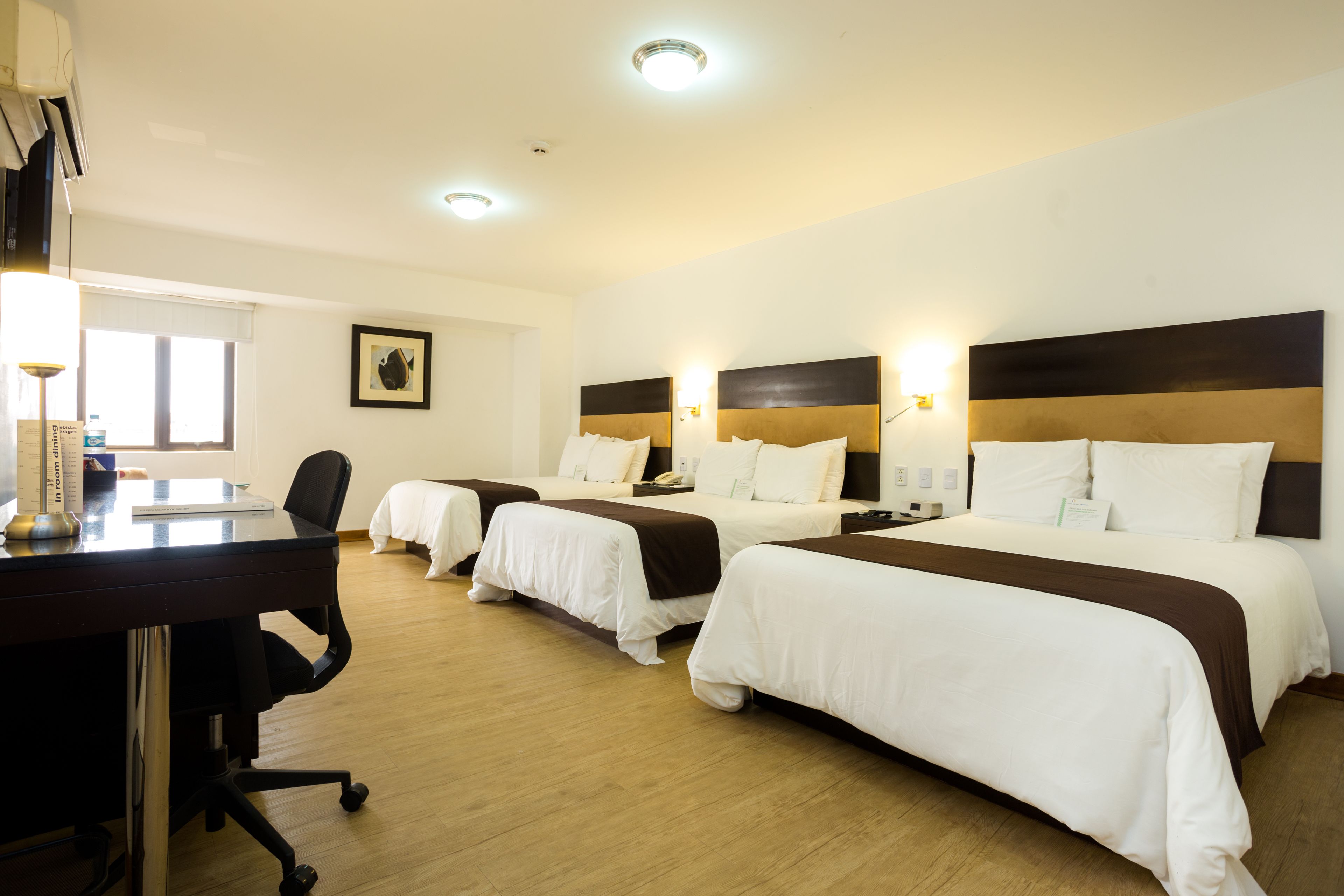 A hotel room with three beds, a desk, and a chair.