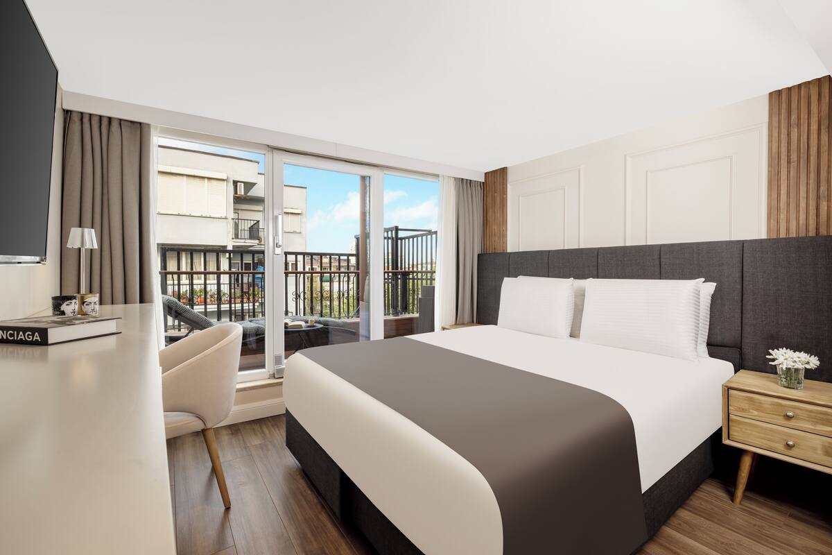 Quarto de hotel moderno com uma cama grande, uma escrivaninha e uma varanda com vista para a cidade.